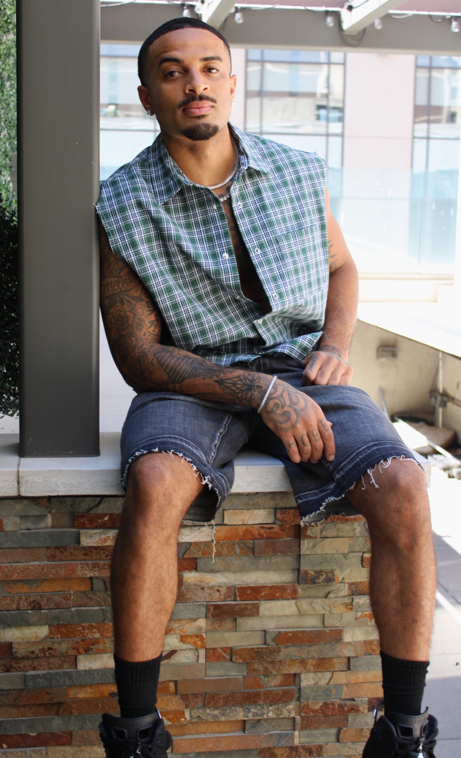 James Muhammad seated commercial fashion portrait in green plaid sleeveless shirt